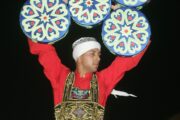 A Tanoura dancer wearing a colorful costume, holding multiple circular props above his head.