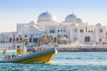 A bright yellow boat passing near a grand, white-domed palace known as Qasr Al Watan.