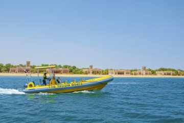 A bright yellow tour boat cruising past fort-like buildings on a desert coastline.