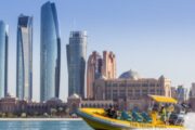 A bright yellow tour boat with passengers, set against Abu Dhabi’s modern skyline including Emirates Palace.