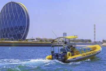 A bright yellow boat passing by the iconic circular Aldar HQ in Abu Dhabi.