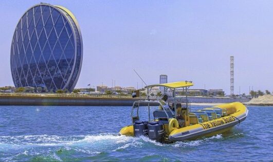 A bright yellow boat passing by the iconic circular Aldar HQ in Abu Dhabi.