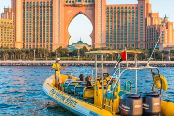 A bright yellow tour boat floating in front of the majestic Atlantis Hotel on Palm Jumeirah.