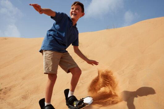 Young boy sandboarding on golden dunes in Dubai