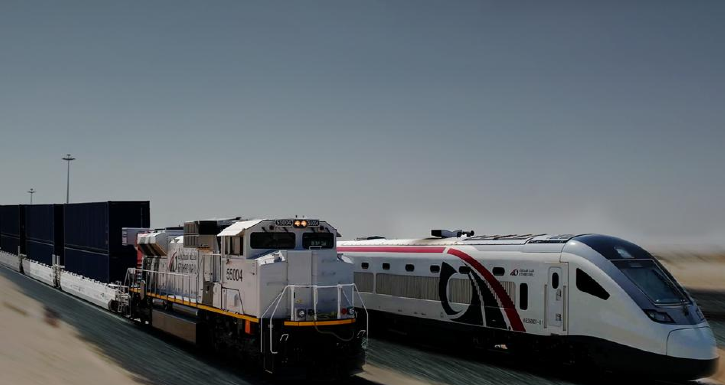 Etihad Rail freight and passenger trains running parallel on desert tracks.