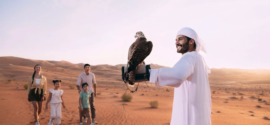 Family enjoying a falconry experience with a local guide in the Al Dhafra desert at sunset.