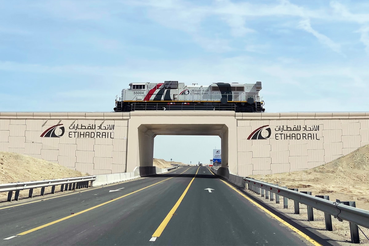 Etihad Rail freight train crossing a modern overpass above a UAE highway.