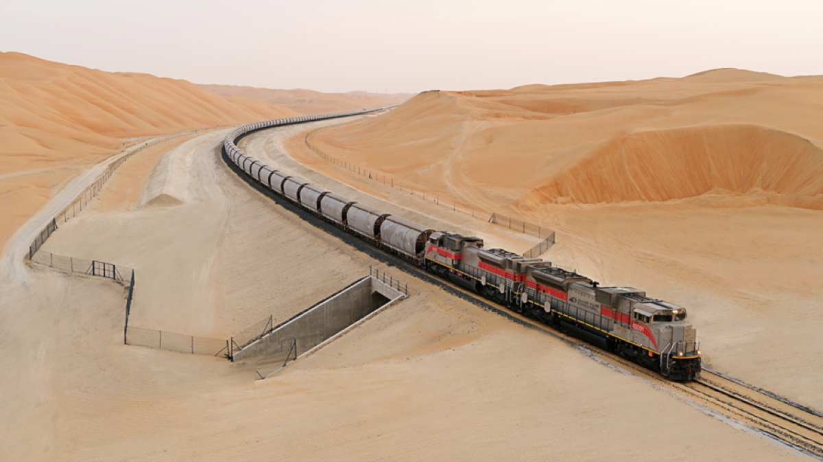 Etihad Rail freight train traveling through vast desert dunes in the UAE.