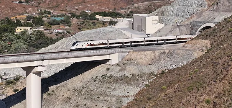 Etihad Rail passenger train crossing a bridge with mountains in the background.