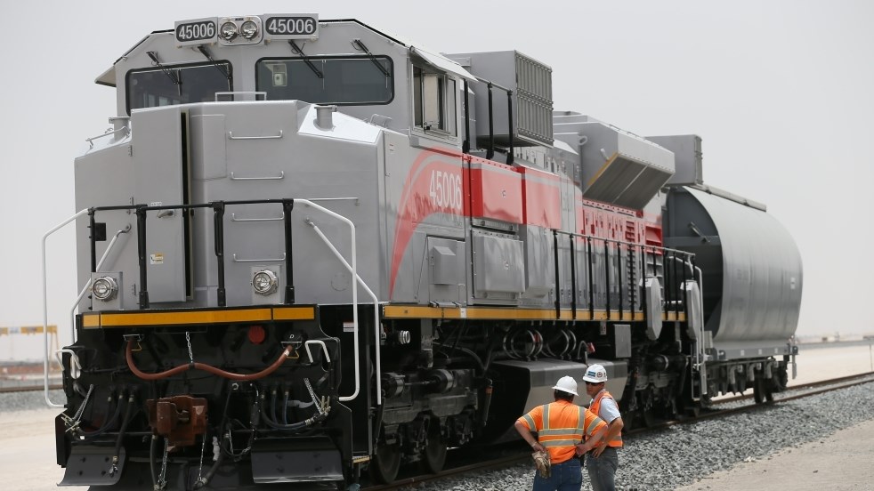 Etihad Rail locomotive with two workers in safety vests standing nearby.