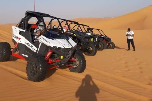 Lineup of Polaris RZR dune buggies parked on the sand during a Dubai desert tour.