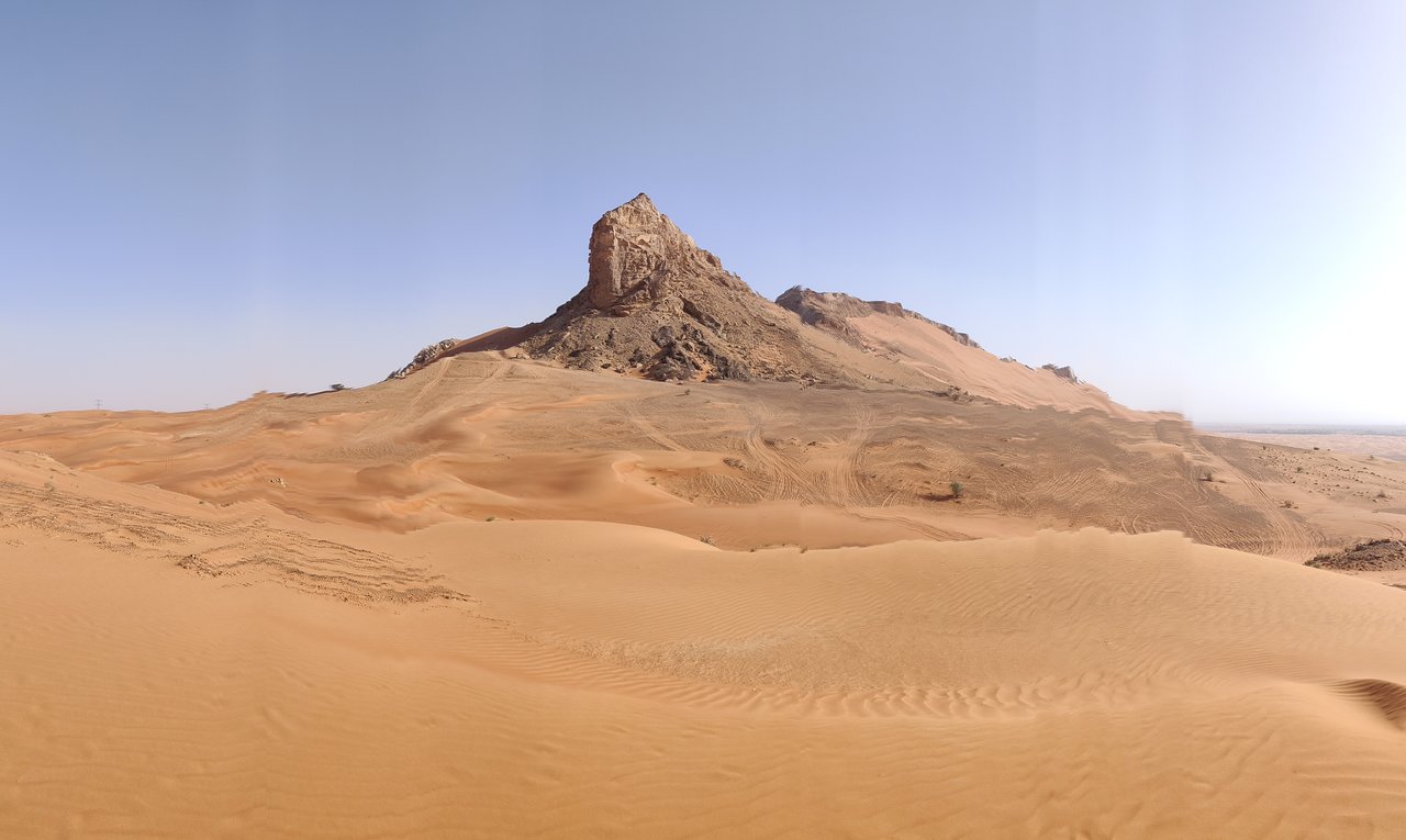 Rocky desert mountain rising from vast sand dunes