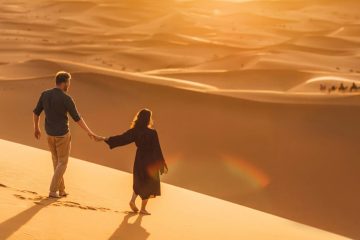 Couple walking hand in hand on sand dunes at sunset