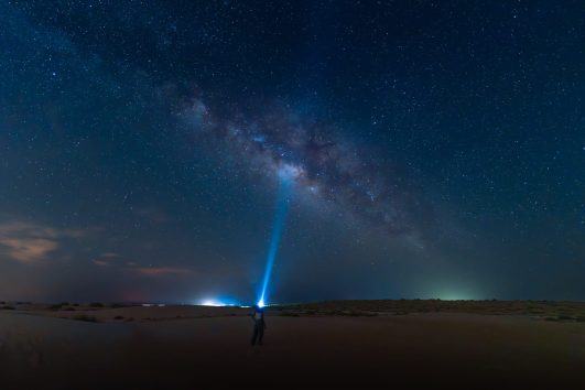 La Via Lattea è visibile sulle dune del deserto degli Emirati Arabi Uniti durante l'osservazione notturna delle stelle con un raggio di luce puntato verso il cielo