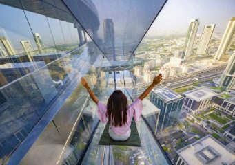 person sliding down glass slide Sky Views Dubai with city skyline view below