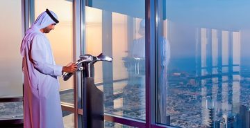 man using binocular viewer Sky Views Observatory Dubai skyline indoor glass windows