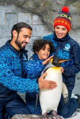 A father, mother, and young child smiling while gently petting a King Penguin at Ski Dubai.