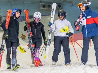 Four young adults laughing and holding their skis and poles while standing on the indoor snow at Ski Dubai.