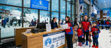 A family of four at the Ski Dubai "Online Booking Counter" picking up their pre-booked gear from a friendly staff member.