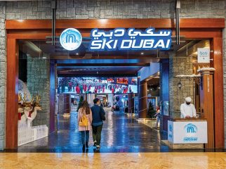 The grand stone-walled entrance of Ski Dubai featuring its blue logo and a couple walking toward the interior.