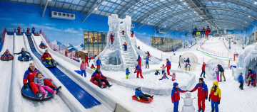 A wide view of the indoor Snow Park featuring family activities like tubing slides, a giant ice castle, Zorb balls, and snowmen.