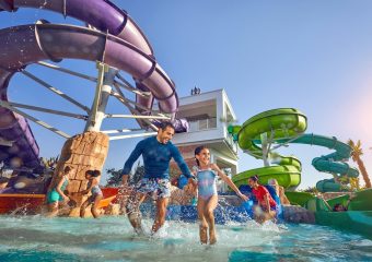 A tall, near-vertical water slide descending from a Mayan-style temple tower into a clear blue pool.