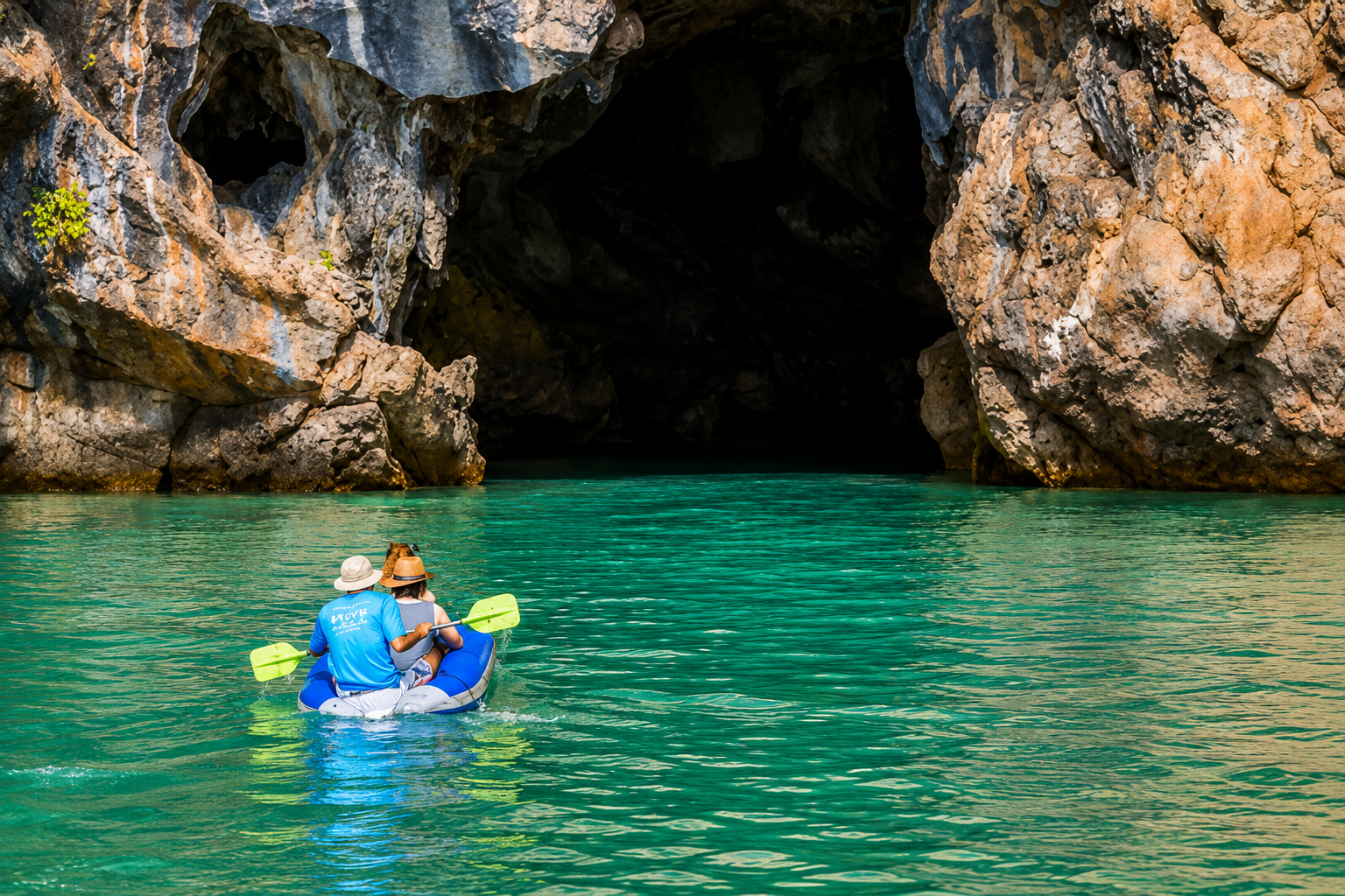 Una coppia in kayak si dirige verso una grotta marina calcarea circondata da acque color verde smeraldo a Krabi.