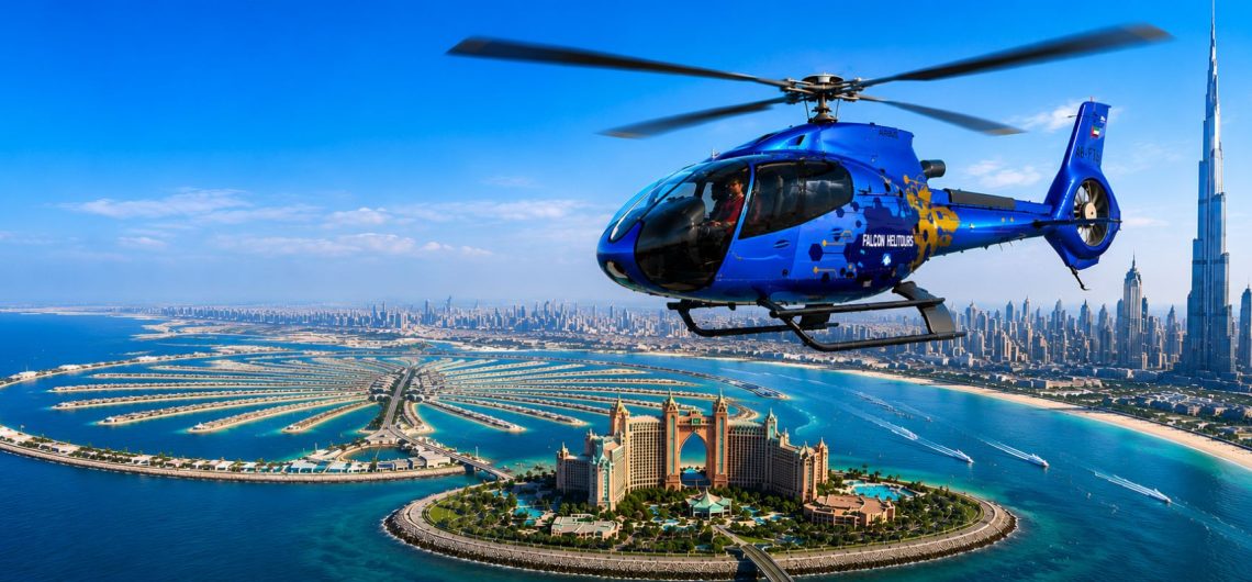 Blue helicopter flying over Palm Jumeirah, Atlantis The Palm and Burj Khalifa during a Dubai helicopter tour with panoramic skyline views.