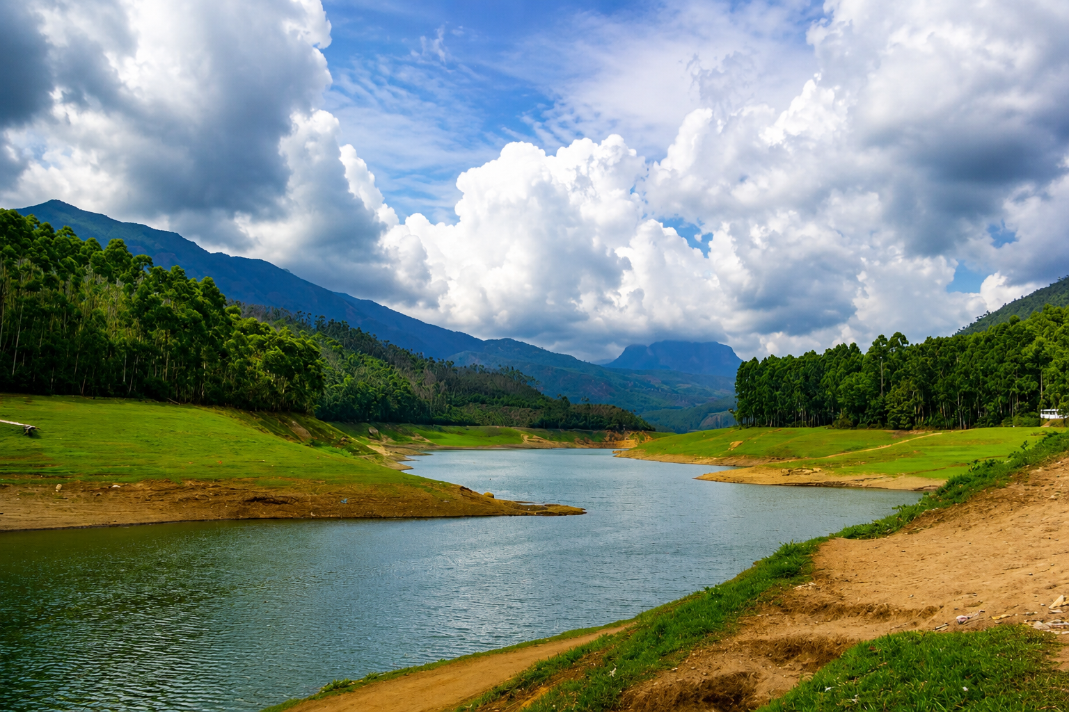 Panoramic view of Echo Point Lake surrounded by forests, rolling hills, and dramatic clouds in Munnar.