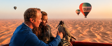Couple enjoying a falcon experience during a hot air balloon ride over the Dubai desert.