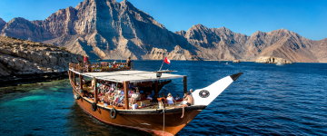 Guests enjoying a traditional Omani dhow cruise through the Musandam fjords surrounded by dramatic mountains.