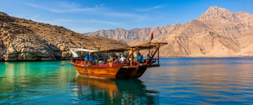 Traditional wooden dhow anchored in the turquoise waters of Musandam with mountain scenery in the background.