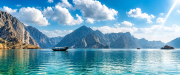 Traditional dhow sailing across the calm turquoise waters of the Musandam fjords surrounded by dramatic mountains.