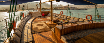 Spacious traditional Omani dhow deck with comfortable seating, dining setup, and panoramic sea views in Musandam.